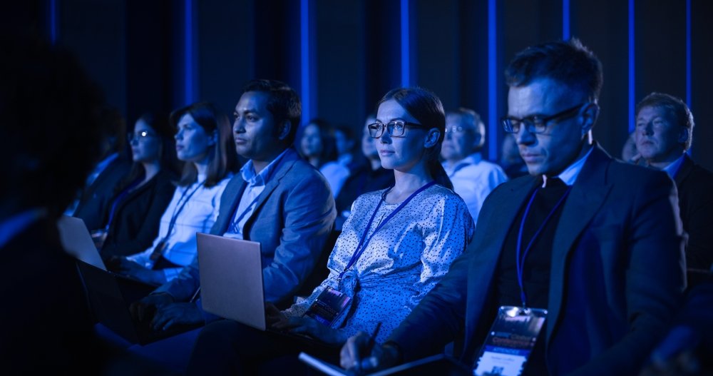 Joven sentada en un público atestado en una conferencia de negocios